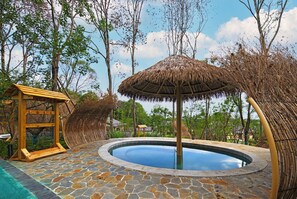 A circular stone pool with a thatched umbrella, surrounded by stone tiles and wooden structures. - Howard Johnson Hot Springs Plaza Yinghuashan (Deyang)