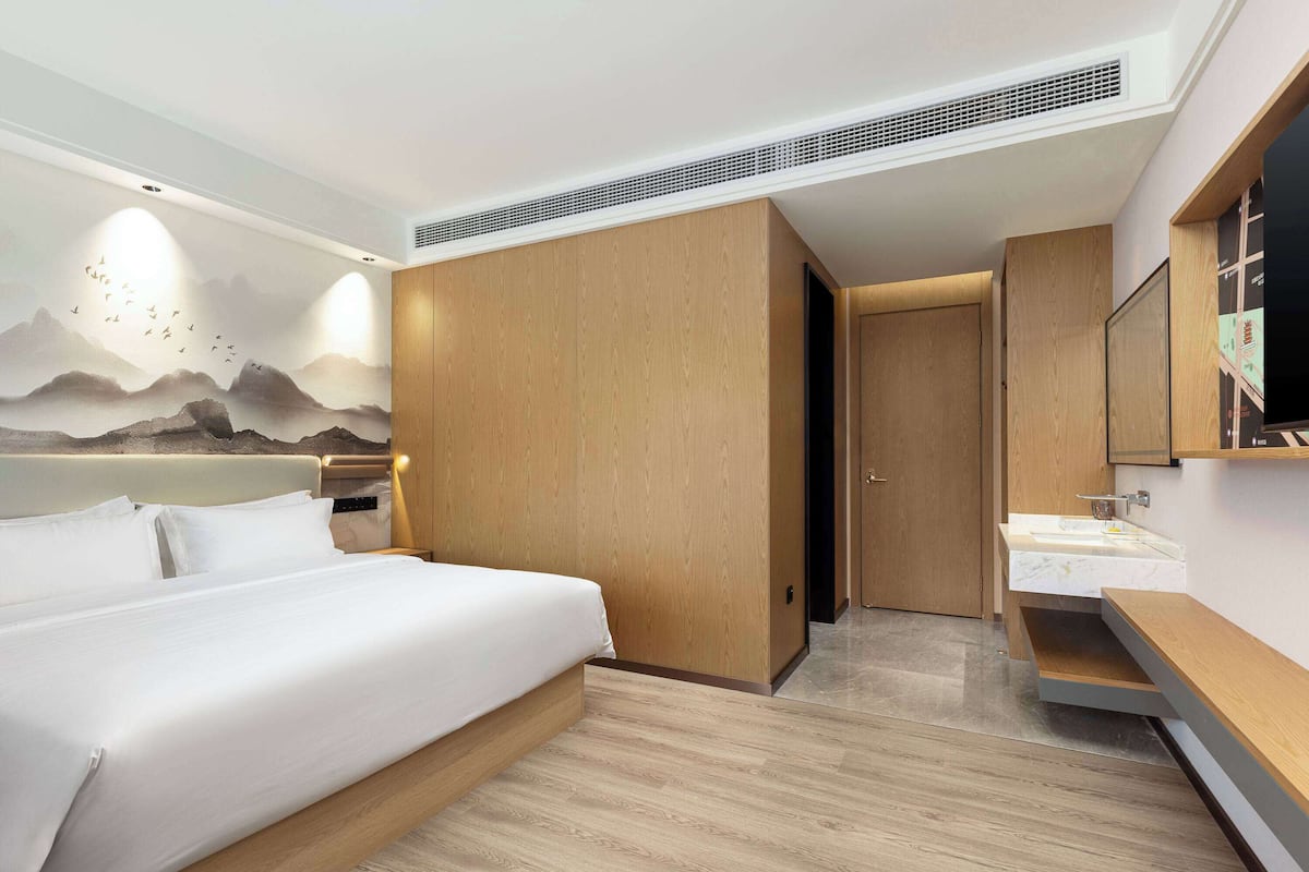 A modern hotel room with a bed, a bathroom with a sink, and a mural of mountains and birds.