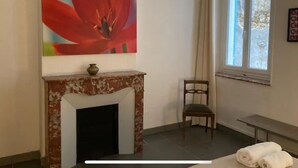 A room with a fireplace, a chair, a bed, and a window with curtains.