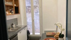 A compact kitchen with a window, a small dining table, and a shelf with kitchenware.
