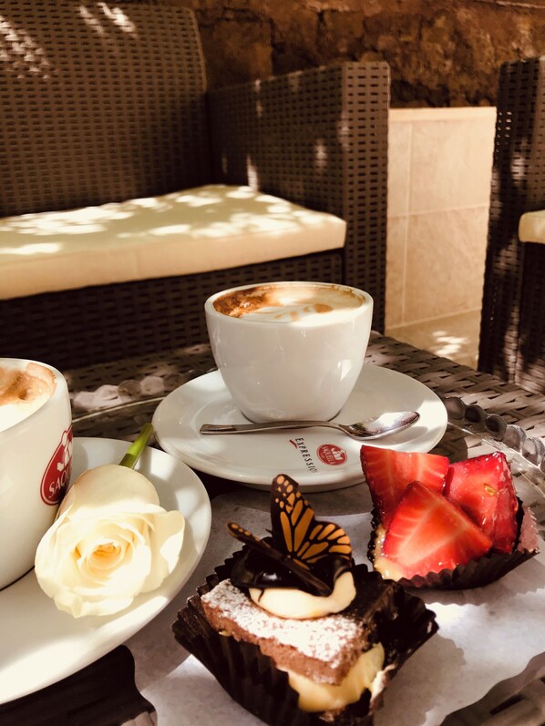 A table with a white cup of coffee, a cake, a rose, and strawberries. - Aruna Suites (Rome)