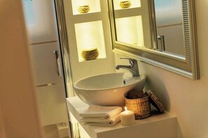 A bathroom with a white sink, a mirror, and a small basket. - Aruna Suites (Rome)