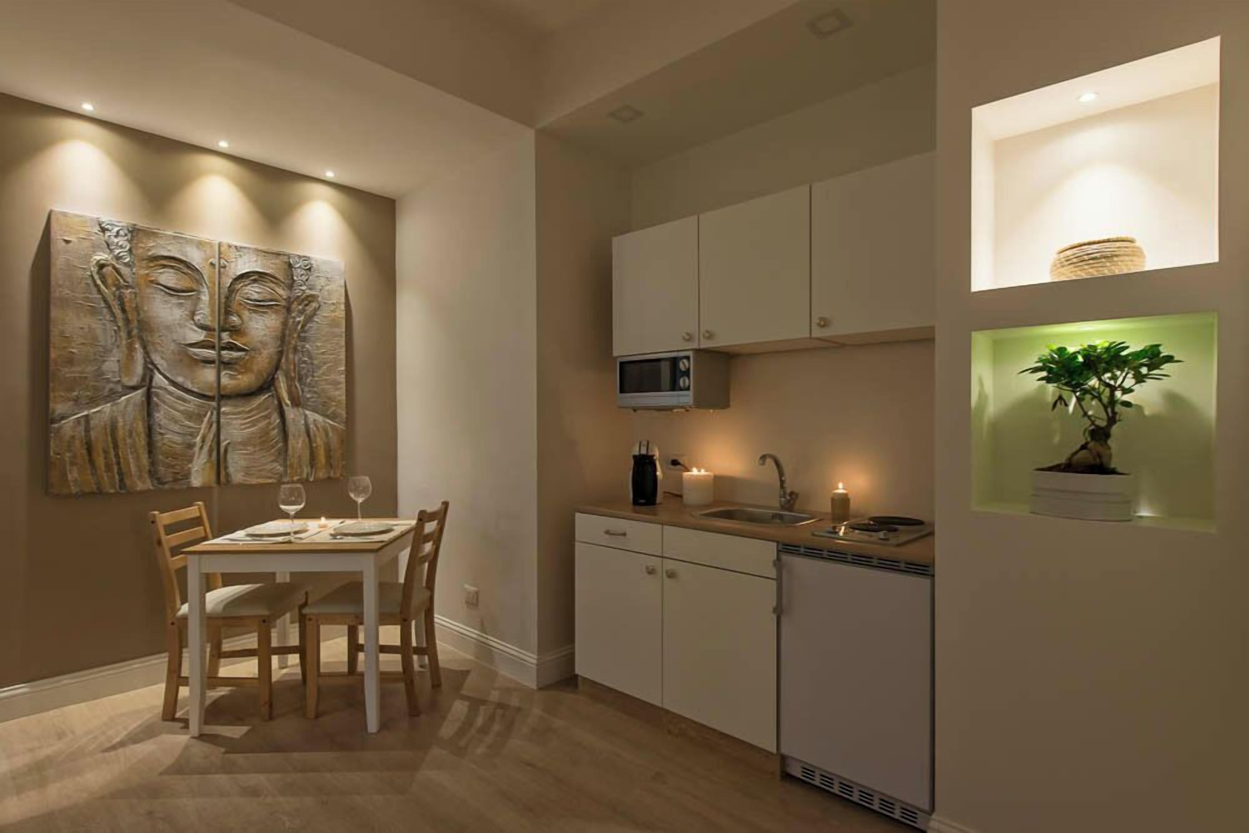 A modern kitchen with white cabinets, a microwave, and a sink. There is a dining table with chairs and a large abstract painting on the wall.