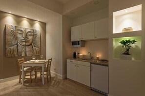 A modern kitchen with white cabinets, a microwave, and a sink. There is a dining table with chairs and a large abstract painting on the wall. - Aruna Suites (Rome)