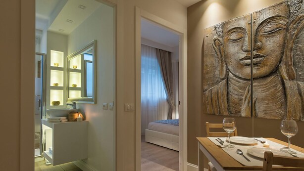 Ein modernes Hotelzimmer mit Essbereich, einer großen Buddha-Statue und einem hell erleuchteten Badezimmer.