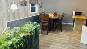 Ein Essbereich mit Holztisch, Stühlen, einem Deckenventilator und einer kleinen Küchenzeile mit einer Mikrowelle.