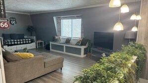 Ein modernes Wohnzimmer mit einer Couch, einer Bank, einem Fernseher und einem großen Fenster.