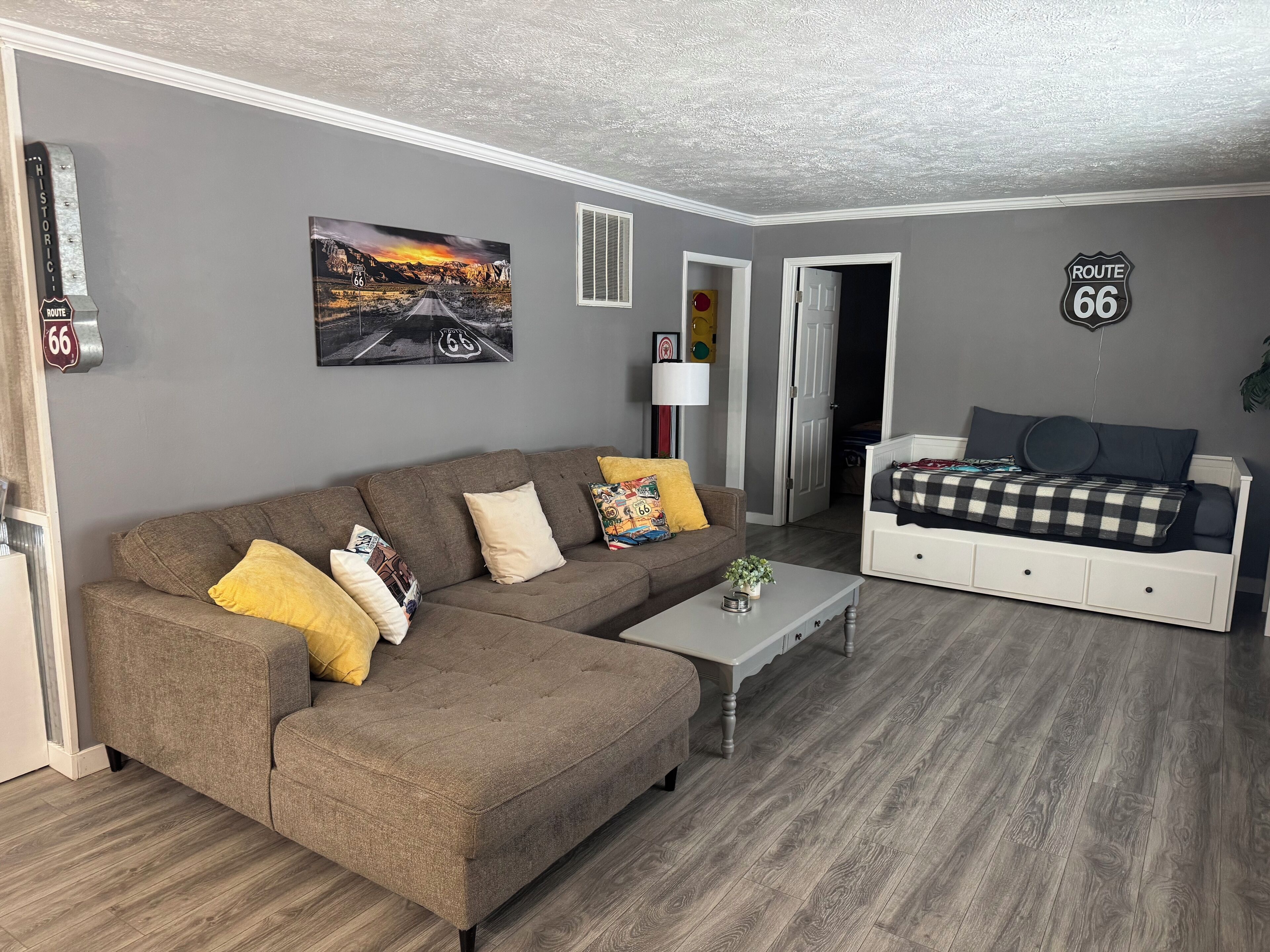 En stue med en brun hjørnesofa, en seng i hvid og vægdekoration med tema fra Route 66.