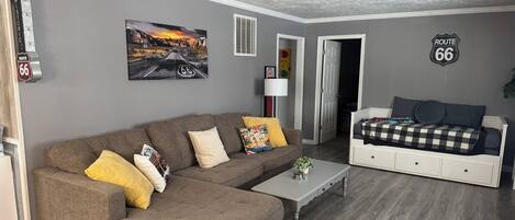 En stue med en brun hjørnesofa, en seng i hvid og vægdekoration med tema fra Route 66.