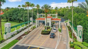 A gated entrance with a red-roofed building, a parking area with cars, and lush greenery. - 3BR Home: Family Retreat Near Disney (Kissimmee)