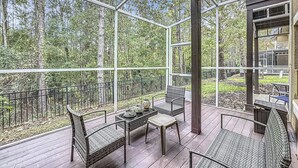 A covered outdoor deck with wicker furniture and a view of a forest. - 3BR Home: Family Retreat Near Disney (Kissimmee)