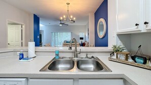A modern kitchen with a double sink, a ceiling fan, and a decorative mirror above the sink. - 3BR Home: Family Retreat Near Disney (Kissimmee)