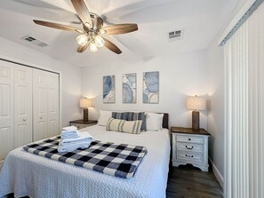 A neatly arranged bedroom with a bed, two bedside tables, a ceiling fan, and artwork on the wall.