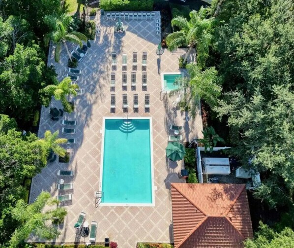 An aerial view of a hotel with a central swimming pool, multiple lounge areas, and surrounding greenery.