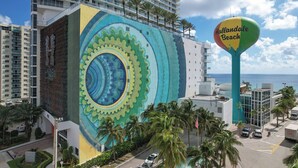 A hotel with a large mural on the side, a view of the sea, and a sign for 'Hollandale Beach'.
