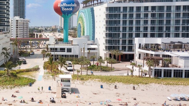A beach with a large water tower labeled 'Hollandale Beach' and a modern hotel with multiple floors and balconies.