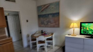 A room with a wooden desk, a chair, a television, a lamp, and a bed with rolled towels.