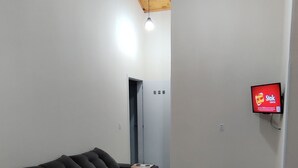 Un salon moderne avec un canapé noir, un plafond en bois et un téléviseur fixé au mur.