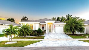 A two-story house with a front driveway, a garage, and a well-maintained lawn with palm trees.