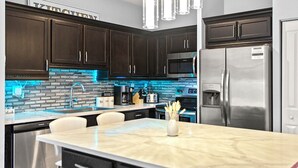 A modern kitchen with dark wood cabinets, stainless steel appliances, a marble island, and blue LED lighting.