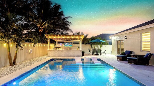 A swimming pool with lounge chairs, a bar area, and a pergola with string lights.