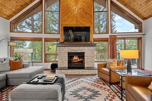 Un salón espacioso con chimenea de piedra, ventanas amplias y techo alto.