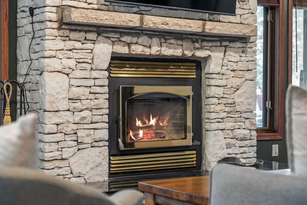 Una chimenea de piedra con fuego a la vista, una repisa de madera y un inserto moderno.