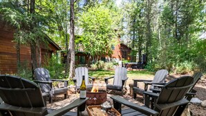 Un espacio al aire libre acogedor con sillas tipo Adirondack, una chimenea y una botella de vino.