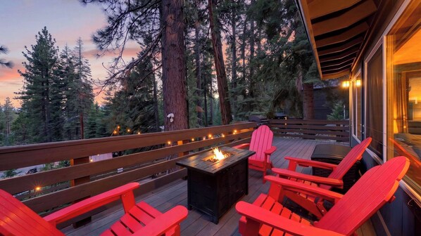 A deck with red Adirondack chairs, a fire pit, and a view of tall trees at dusk. - Washoe Way by Avantstay Luxury Tahoe Retreat A+ Location w/ Beach Access (Tahoe City)