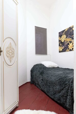 A bedroom with a bed, a wardrobe, a window, and a wall with a tropical leaf pattern.