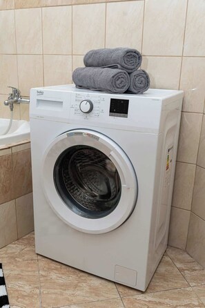Une machine à laver à chargement frontal, dotée d’un panneau de commande, d’un écran numérique et d’un compartiment à chargement par le dessus.