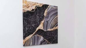 A room with a black sofa and a marble-patterned artwork on the wall.
