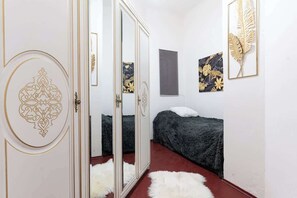 Une chambre avec une armoire à portes miroir, un lit recouvert d’une couverture sombre et deux œuvres d’art représentant des feuilles, encadrées et accrochées au mur.