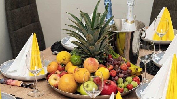 A dining table set with plates, cutlery, and a fruit platter.