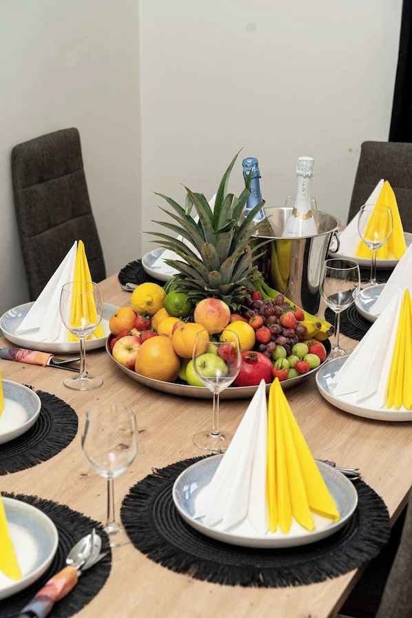 Uma mesa de jantar posta com pratos, talheres e uma travessa de frutas.