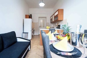 Um espaço compacto com cozinha americana, área de refeições com mesa posta para dois e um sofá.