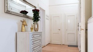 A hallway with a white dresser, a mirror, and a vase of red flowers. There are two white doors and a radiator on the right.