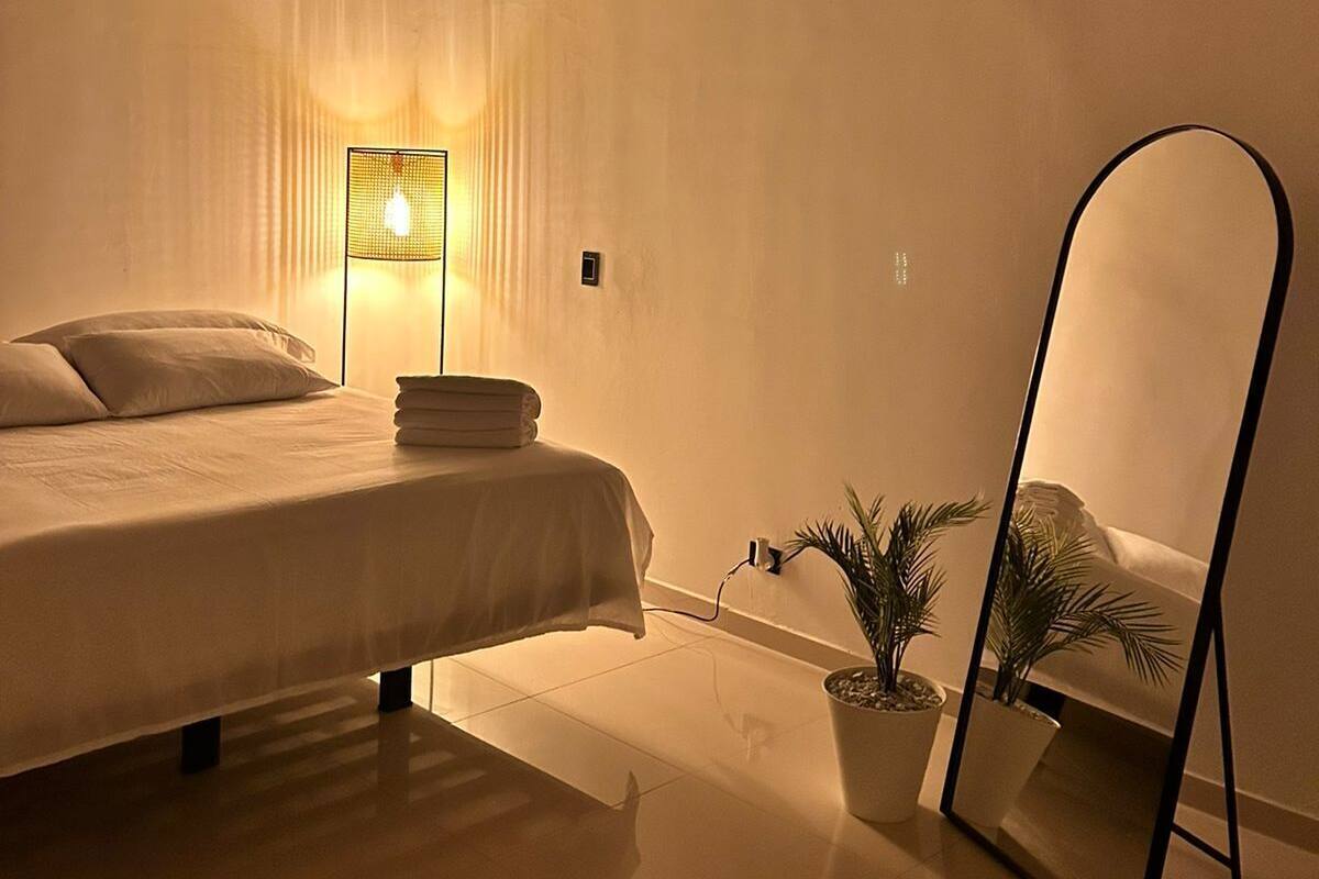 A bedroom with a bed, bedside lamp, air conditioning unit, and a mirror.