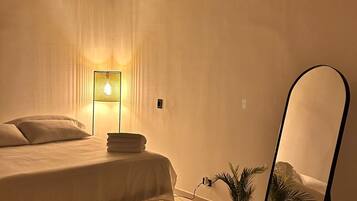 A bedroom with a bed, bedside lamp, air conditioning unit, and a mirror.