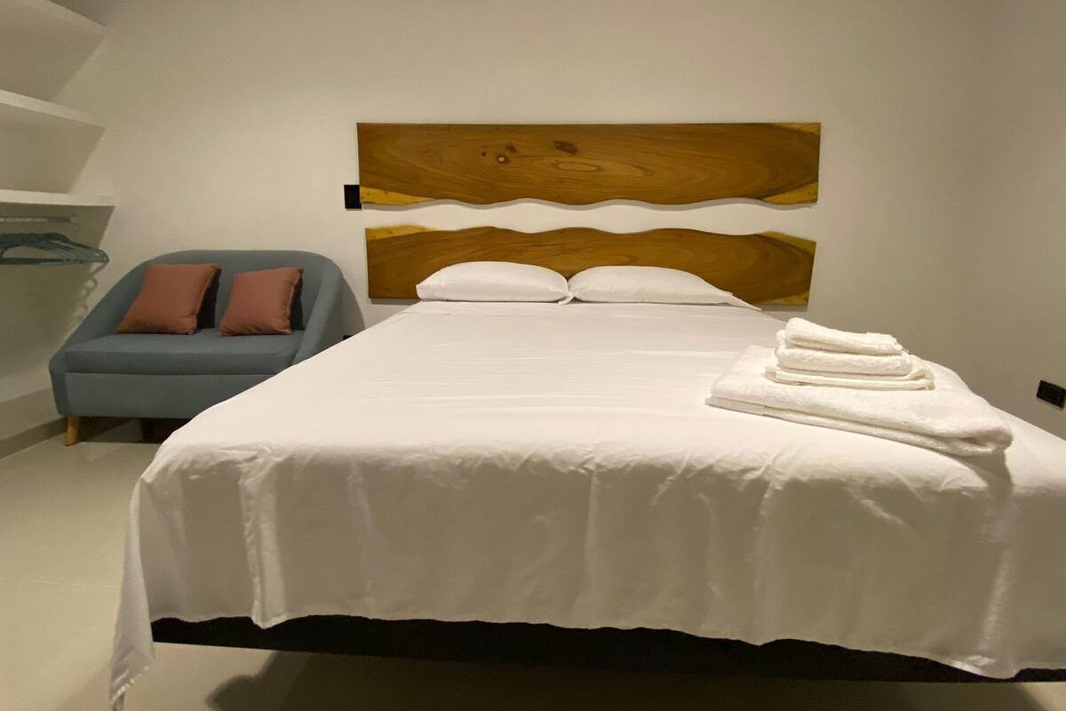 A neatly made bed with white linens, a wooden headboard, and a stack of white towels on the side.