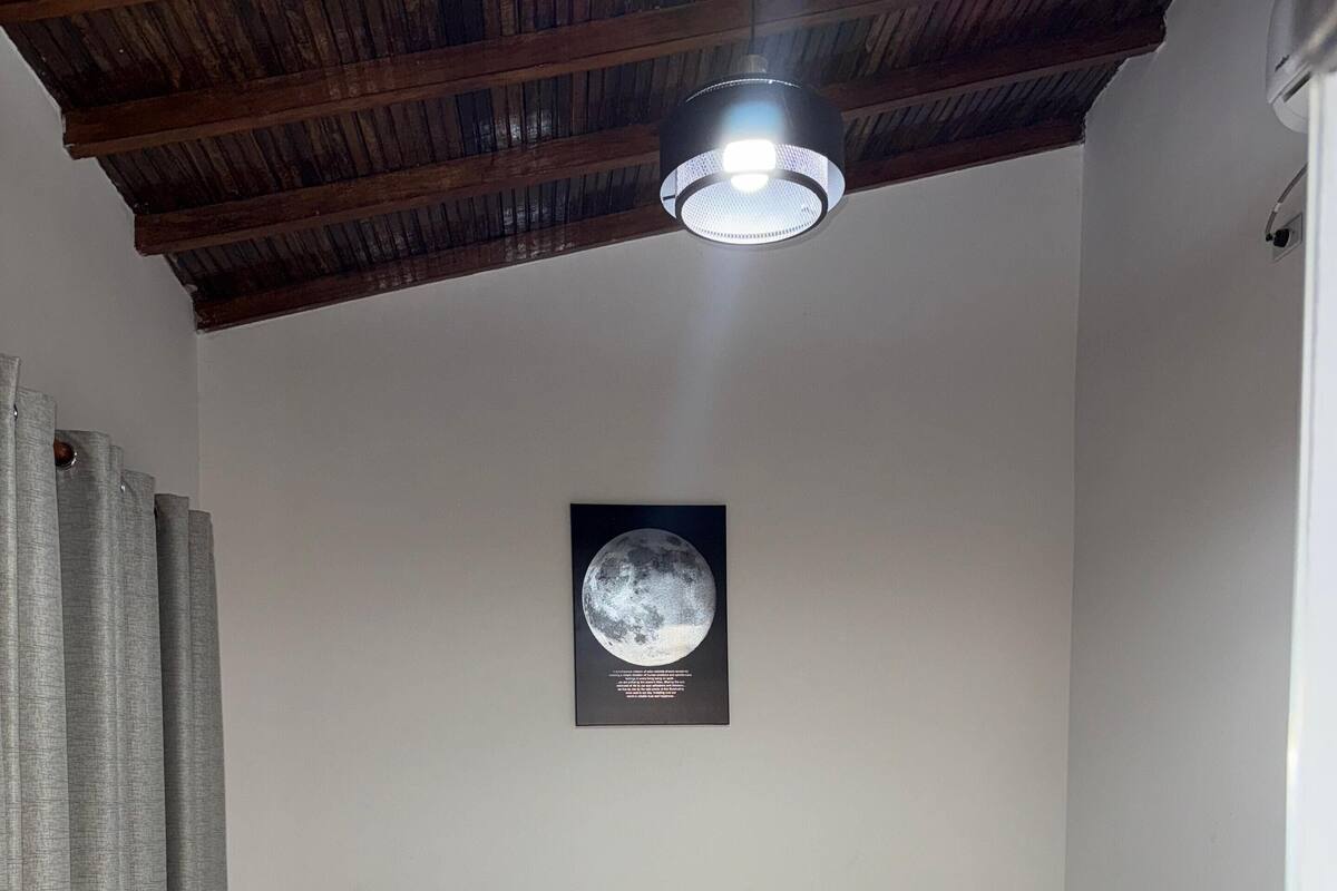 A bedroom with a bed, a nightstand, a wall-mounted lamp, and a framed picture of the moon.