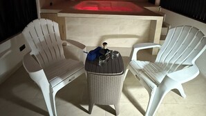 Een overdekt terras met twee witte stoelen, een rieten tafel en een ingebouwd whirlpool.