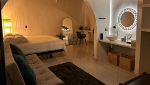 Een moderne slaapkamer met een bed, een bank, een bureau en een badkamer met spiegel en wastafel.