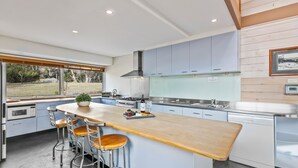 A modern kitchen with a central island, bar stools, stainless steel appliances, and a view of the outdoors. - Silvertop Apartment capturing the beautiful mountain and lake views (Crackenback)