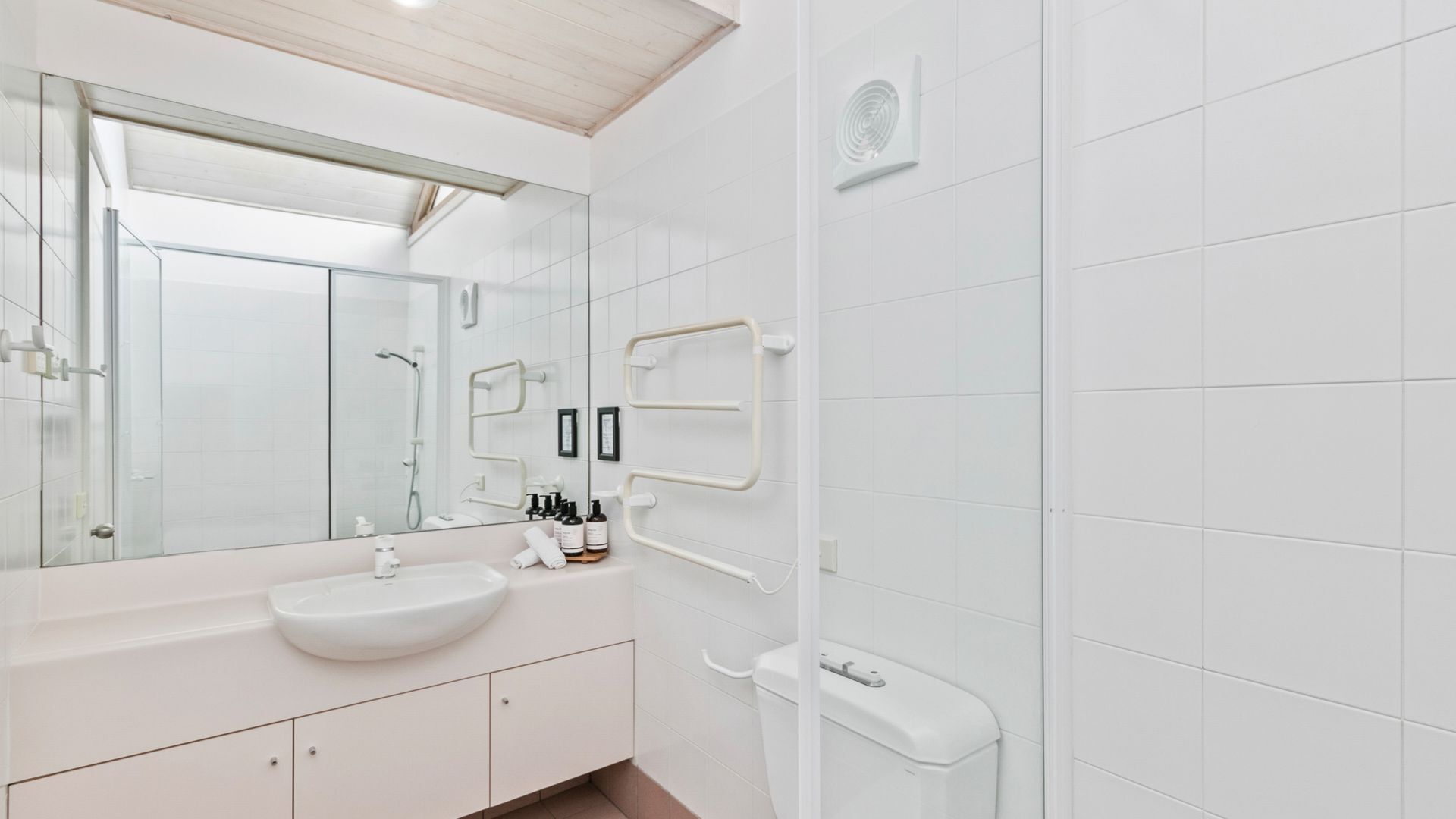 Une salle de bain moderne avec un grand miroir, des carreaux blancs, un lavabo et des toilettes.