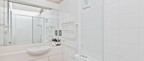 Une salle de bain moderne avec un grand miroir, des carreaux blancs, un lavabo et des toilettes.