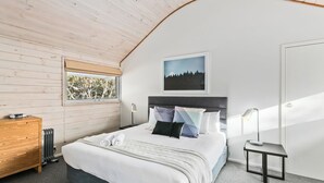A bedroom with a bed, a nightstand, a wooden dresser, a window with a view, and a framed picture on the wall. - Silvertop Apartment capturing the beautiful mountain and lake views (Crackenback)