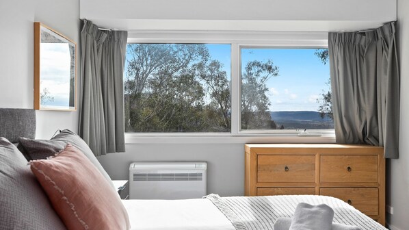 A bedroom with a bed, a dresser, a window with curtains, and an air conditioning unit. - Silvertop Chalet is ideal for large families and groups of friends (Crackenback)