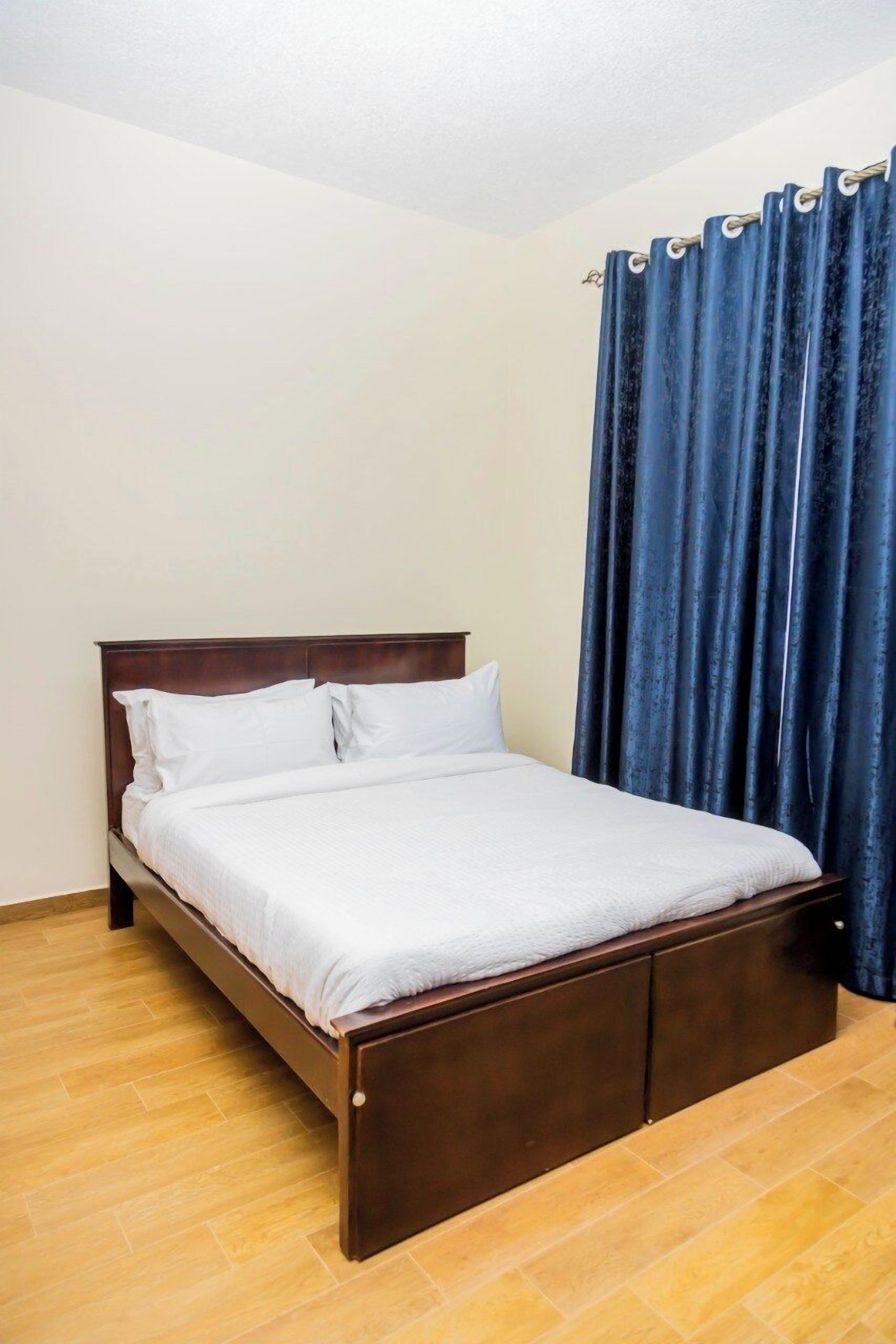 A single bed with a wooden frame and white bedding in a room with light-colored walls and wooden flooring.