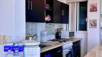 A modern kitchen with dark cabinets, a microwave, a stove, and a sink. There are water bottles and a Kirkland brand package on the counter.